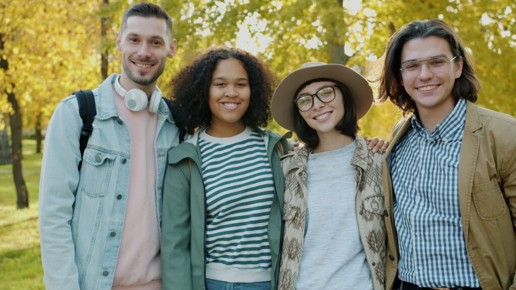 Four friends smiling together in a park during a sunny fall day.